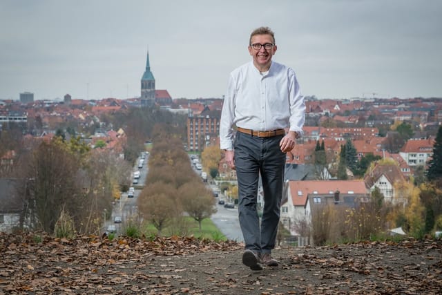 Matthias Brinkmann schreitet vor Hildesheims Stadtpanorama fröhlich in Richtung entgegen.